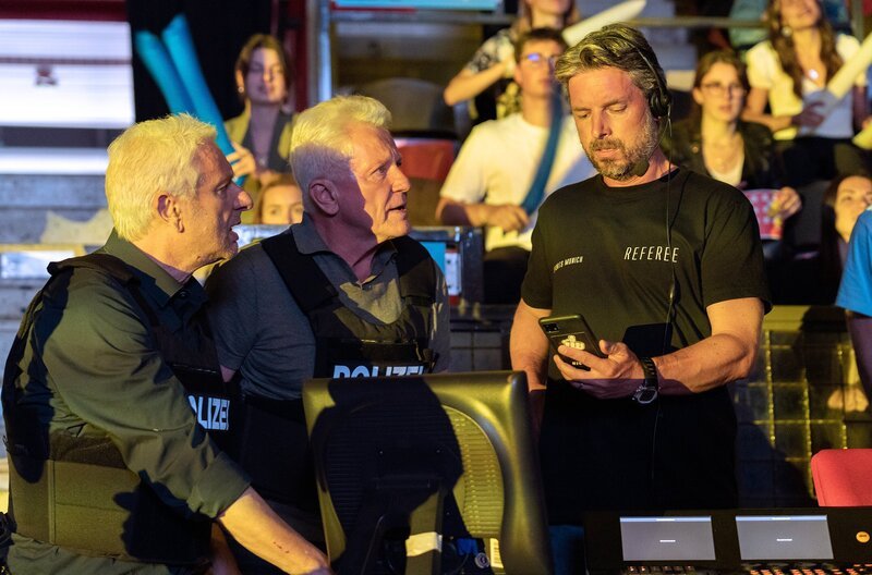 Von links: Franz Leitmayr (Udo Wachtveitl) und Ivo Batic (Miroslav Nemec) zeigen Referee (Danny Rosness) ein Foto in der Arena. – Bild: BR/​Bavaria Fiction GmbH/​Claudia Milutinov