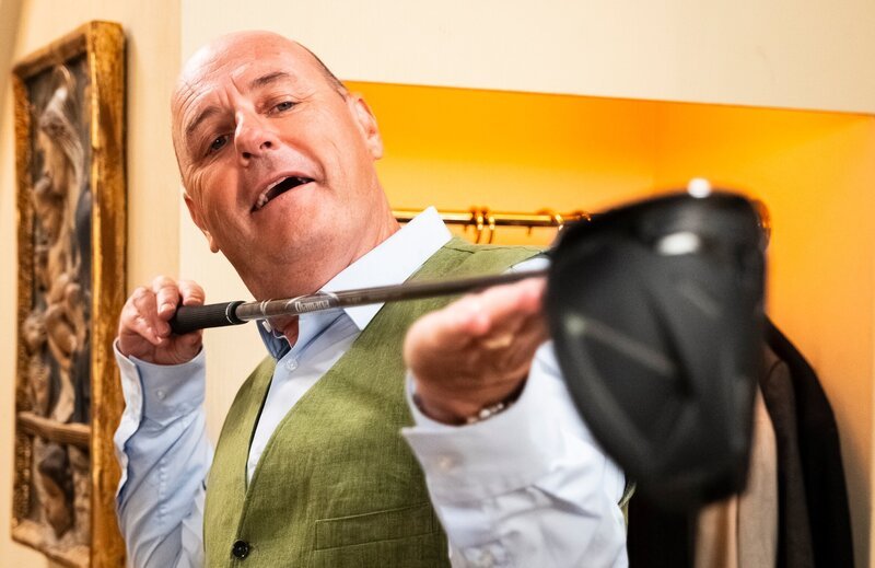 Hubert (Bernhard Ulrich) freut sich über den neuen, teuren Golfschläger, den er sich gekauft hat. – Bild: BR/​Lena Semmelroggen