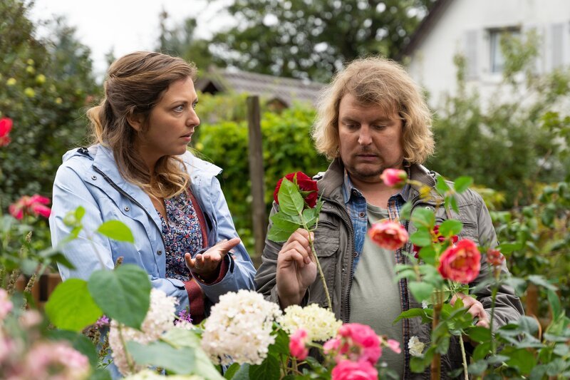 Um eine freie Parzelle in der Schrebergartenkolonie zu bekommen, will Xaver Frühweiss (Franz-Xaver Zeller, r.) Frau Grasegger mit frisch gepflückten Blumen beeindrucken, wovon seine Freundin Katja Ostermeier (Mira Huber, l.) wenig begeistert ist. – Bild: ZDF und Linda Gschwentner