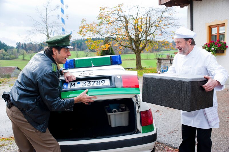 Staller (Helmfried von Lüttichau, links) lässt sich vom Koch des Gasthofs „Ludwig“ Erwin Sauer (Karl Fred Müller) das Essen in den Kofferraum stellen. – Bild: Leonine /​ Chris Hirschhäuser /​ Marco Meenen /​ ARD /​ Entertainment Factory GmbH