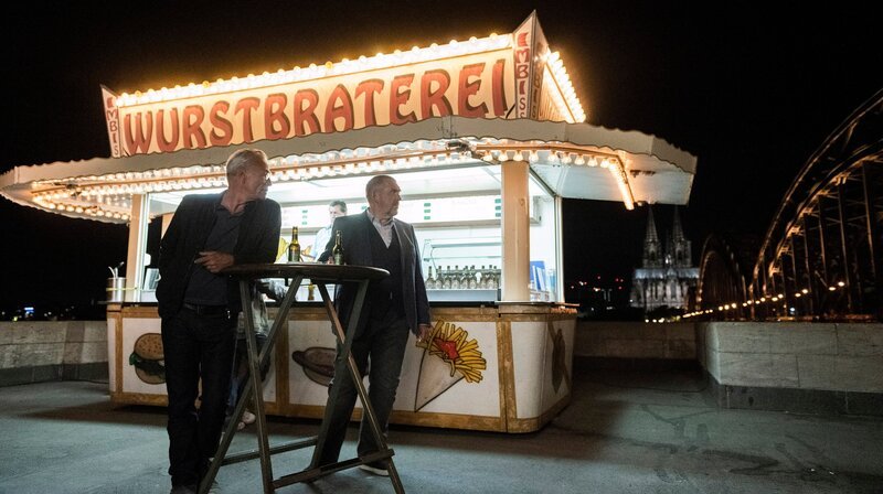 Feierabend an der Wurstbraterei: Freddy Schenk (Dietmar Bär, rechts) und Max Ballauf (Klaus J. Behrendt, links) mit dem Dom und der Deutzer Brücke. – Bild: WDR/​Martin Valentin Menke