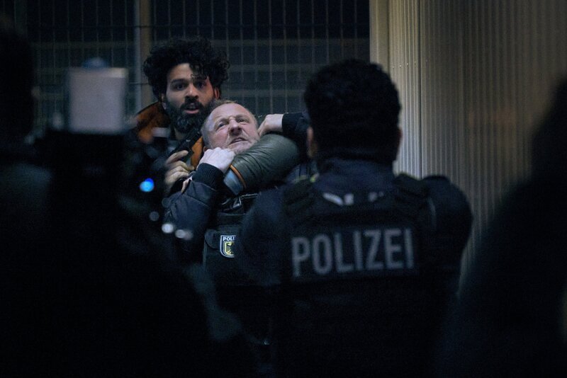 Joon Rostami (Altamasch Noor, l.) bedroht Roland Orbach (Maximilian Brückner, M.) mit der Waffe. Jalil (Aziz Dyab, r.) steht mit gezogener Waffe vor Ihnen. – Bild: ZDF und Nik Konietzny