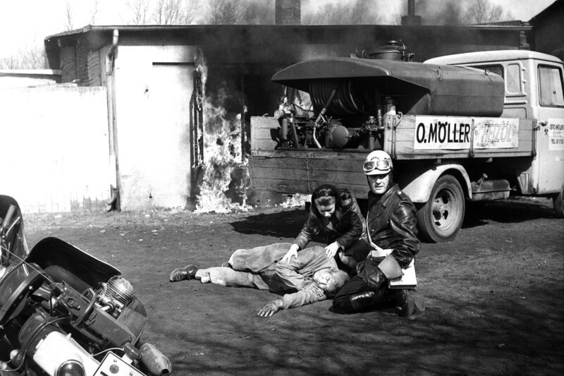 Mutig hat der Streifenfahrer Hartmann (Karl-Heinz Heß, rechts) den Heizölfahrer Berthold (Hans Schellbach) aus der brennenden Baracke gerissen. Gaby Möller (Jutta Kästel), die Tochter des Firmenchefs, bemüht sich um den verletzten Fahrer. – Bild: NDR/​Klügel
