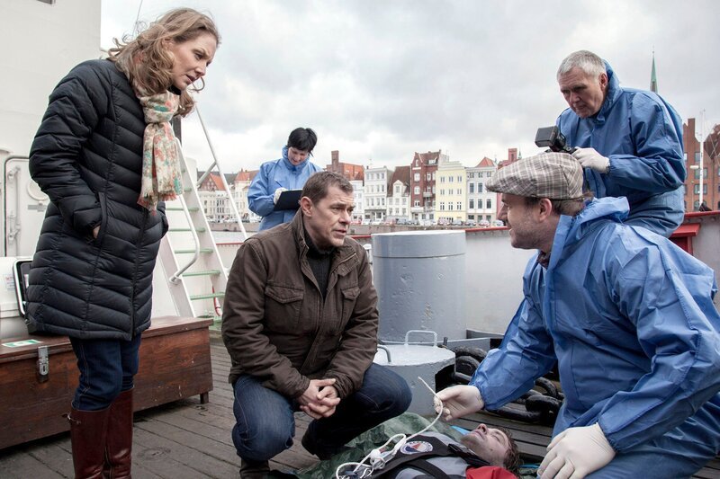 ARD HEITER BIS TÖDLICH – MORDEN IM NORDEN, II. Staffel der Krimiserie am Vorabend mit 16 neuen Folgen, Folge 30 „Über Bord“ am Dienstag (02.07.13) um 18:50 Uhr im Ersten. Die Besatzung eines Feuerwehrschiffs (Komparsen) hat einen Toten aus dem Wasser gezogen. Pathologe Dr. Strahl (Christoph Tomanek, r.) erklärt Finn (Sven Martinek, M.) und Elke Rasmussen (Tessa Mittelstaedt, l.), dass es kein Unfall war, sondern dass es sich um Mord handelt: an einem Sicherungsseil wurde manipuliert. – Bild: ARD/​Georges Pauly