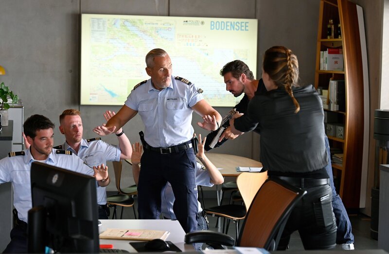 Jakob Frings (Max König, l. mit Komparse) und Paul Schott (Tim Wilde, 3.v.l.) werden von Anatol (Benjamin Piwko, 2.v.r.) und Shiba (Tatiana Nekrasov, r.) als Geiseln genommen. – Bild: ORF/​Bavaria/​ARD/​SWR/​Laurent Trümper