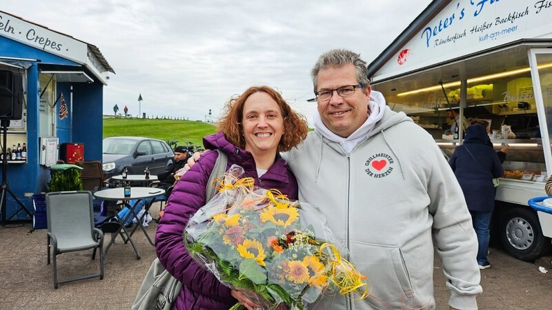 Auf und davon – Schweizer Auswanderer – Wiedersehen an der Nordsee: Brigitte und Sacha Kunz mit Blumenstrauss 2026. – Bild: SRF