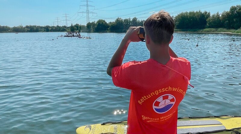 Rettungsschwimmer-Novize Misha Kurinnyi hat sie fest im Blick: Die Badeinsel am Allermöher See ist weiter weg, als gedacht. Häufigste Ursache für Einsätze auf dem Wasser: Die Rettung ermüdeter Schwimmer, die die Entfernung unterschätzt haben. – Bild: NDR Rettungsschwimmer-Novize Misha Kurinnyi hat sie fest im Blick: Die Badeinsel am Allermöher See ist weiter weg, als gedacht. Häufigste Ursache für Einsätze auf dem Wasser: Die Rettung ermüdeter Schwimmer, die die Entfernung unterschätzt haben. – Bild: NDR