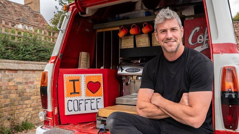 ant anstead, wearing black tshirt and jeans, sitting with arms crossed in the back of the ford transit van AFTER it has been converted to a coffee truck, with machine and coffee cups and sign in view, parked infront of the farm brick wall – Bild: Warner Bros. Discovery
