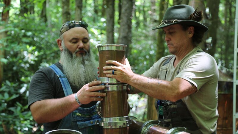 Jerry Benson and Mike Cockrell working on the aged whiskey still in the woods. – Bild: Warner Bros. Discovery