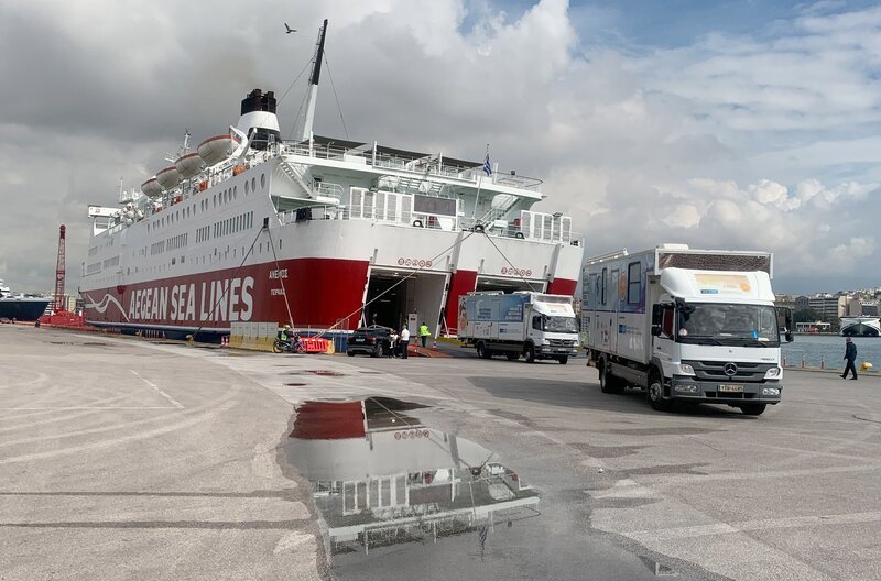 In Piräus gehen zwei LKW beladen mit modernstem medizinischen Equipment an Bord einer Fähre zur Insel Serifos. – Bild: WDR /​ Manuel Gogos
