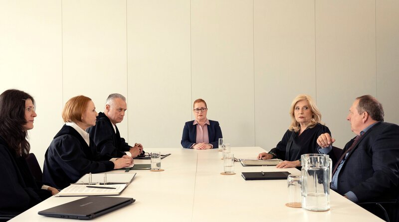 Isabel von Brede (Sabine Postel, 2.v.r.) verteidigt Richter Greinert (Thomas Kügel, r.), dem vorgeworfen wird, er arbeite zu langsam und schaffe viel weniger Fälle als seine Kollegen (Komparsen) vor Richterin Böge (Birgit Berthold, 2.v.r.) und Sonja Ziedrich (Nadja Engel, M.). – Bild: ARD/​Christine Schroeder