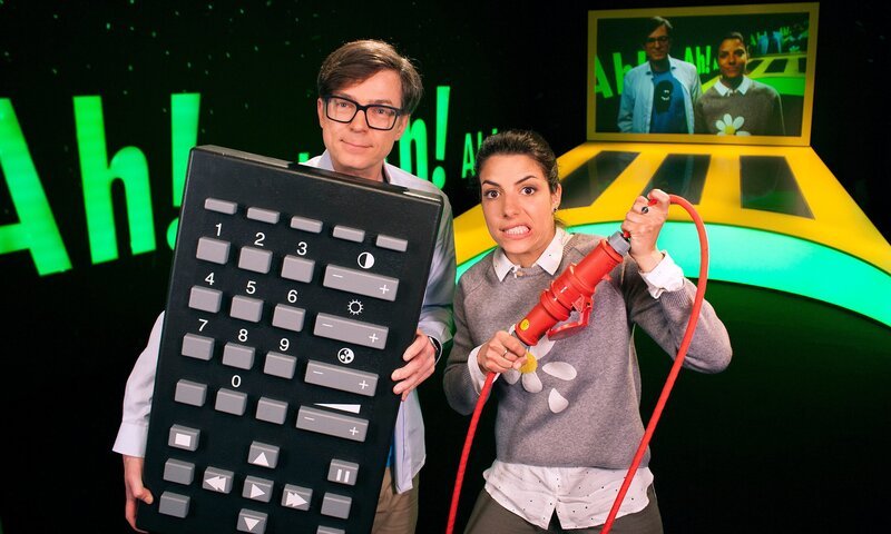 Clarissa und Ralph stehen pünktlich zu Sendungsbeginn im „Wissen macht Ah!“-Studio, aber irgendetwas stimmt nicht. Clarissa kann Ralph nicht sehen und nicht hören. Mit einer riesigen Fernbedienung versucht Ralph, die Sendung anzuhalten. – Bild: WDR/​Thorsten Schneider