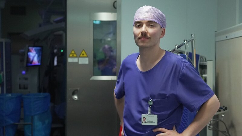 Emre steht vor einem Operationssaal. – Bild: SRF