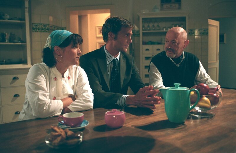 Oliver (Patrik Fichte, M.) teilt Köchin Bärbel (Birgit Wiedel Weidinger, l.) und Verwalter Georg (Uwe Zerbe, r.) mit, dass seine Verlobte früher zurückkehrt. – Bild: ZDF und Britta Krehl