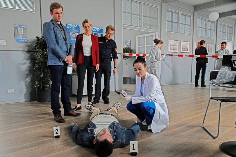 Die Kommissare Thomas (Moritz von Zeddelmann, l.) und Laura Schmidt (Marija Kovčo, 2.v.l.) sowie Polizeihauptmeister Mohr (Max Müller, 3.v.l.) staunen nicht schlecht, als ihnen Rechtsmedizinerin Atay (Sevda Polat, r.) nach ihrer ersten Untersuchung mitteilt, dass das Opfer (Komparse, M.) mit Atropin vergiftet worden ist. – Bild: ZDF/​Saskia Pavek