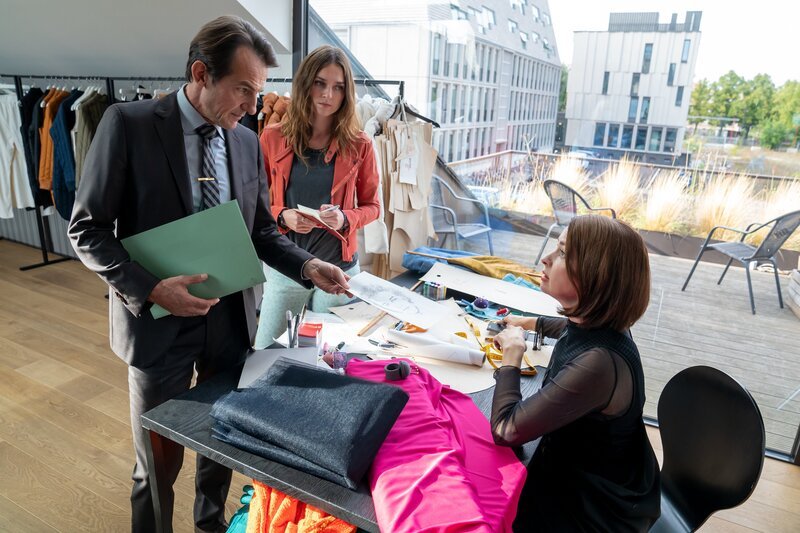 Die Designerin Leah Wörner (Loretta Stern, r.) gibt Radek (Hans-Werner Meyer, l.) und Lucy (Josephin Busch, M.) gegenüber zu, dass sie Probleme mit ihrem ehemaligen Geschäftspartner, dem Designer Michael Pohl, hat. – Bild: Oliver Feist /​ ZDF und Oliver Feist