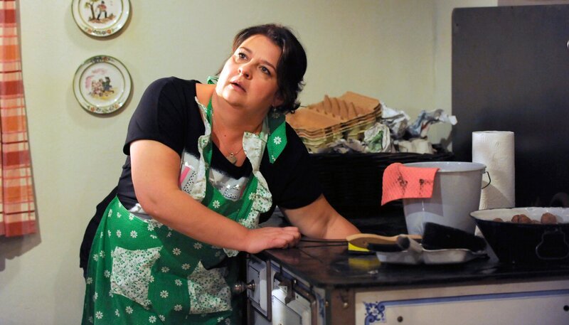 DAHOAM IS DAHOAM, Folge 1436, ‚Klappe zu, Monika steckt‘. Ausgerechnet kurz vor ihrem Scheidungstermin, bleibt Moni (Christine Reimer) mit ihrem Armkettchen am Ofenrost hängen. – Bild: BR/​Marco Orlando Pichler