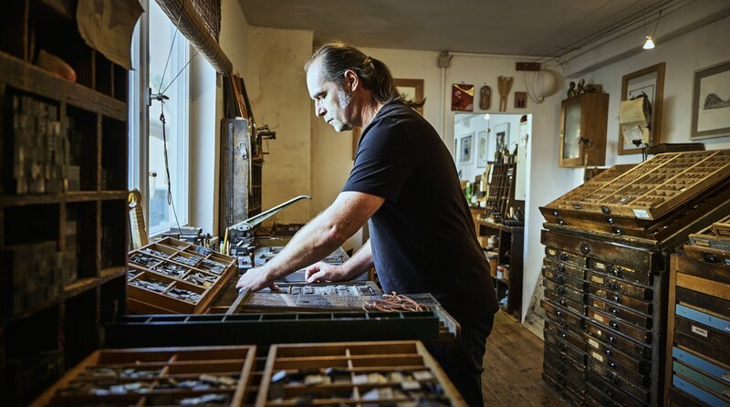 Timo Reger, der Setzer. Er bringt die Motive und Layouts in eine druckbare Form. – Bild: BR/​Pascal Hoffmann