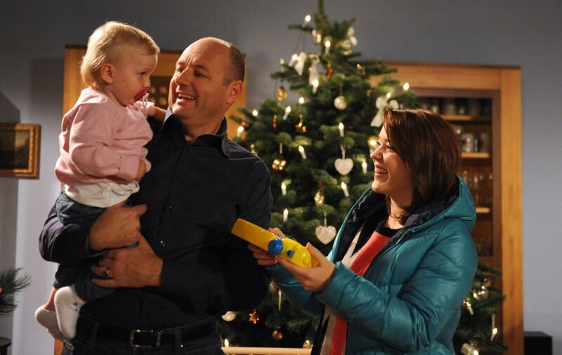 Sogar von Kathi bekommt die kleine Franzi ein Weihnachtsgeschenk. Von links: Franzi, Hubert Kirchleitner (Bernhard Ulrich) und Katharina Benninger (Carina Dengler). – Bild: BR/​Marco Orlando Pichler