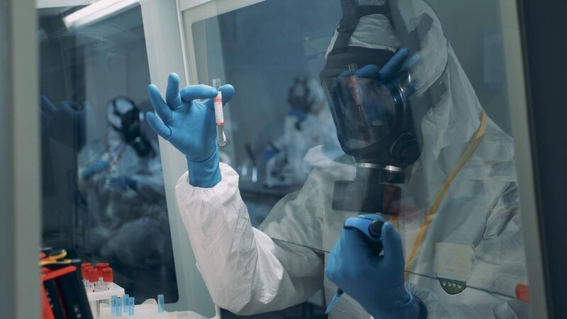 Ein Labortechniker schüttelt ein Reagenzglas hinter einer Schutzscheibe in einem BSL-Labor. – Bild: RTL