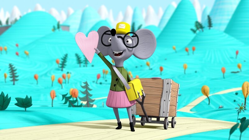 Henrietta, die Postbotin, winkt fröhlich mit einer Valentinstagskarte. – Bild: NDR/​Autour de Minuit Productions/​France Télévisions/​Borderline Films