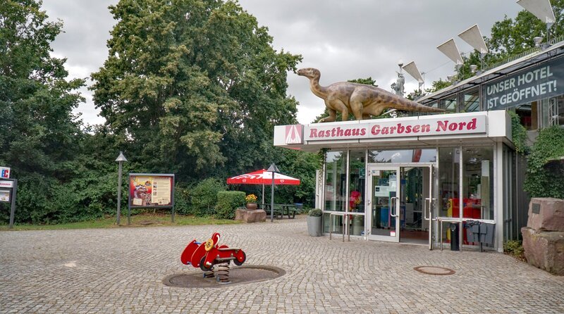NDR Fernsehen DIE NORDREPORTAGE: STAU, STRESS UND PANNENDIENST, "Ferienstart auf der Autobahn", am Mittwoch (19.08.26) um 18:15 Uhr. 72 Jahre, mit Hotel und Dino auf dem Dach: Garbsen Nord ist eines der bekanntesten Autobahn-Rasthäuser in Norddeutschland – Bild: NDR