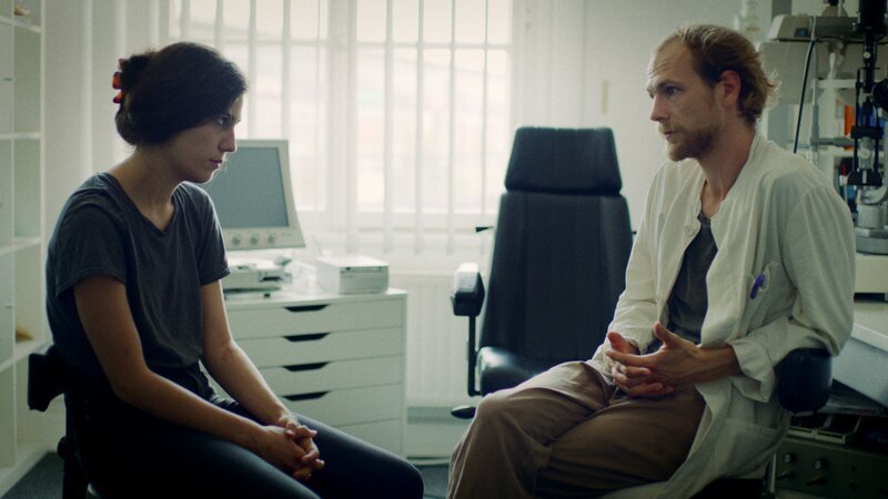 Jona (Naomi Achternbusch) will vom Augenarzt (Robert Gwisdek) wissen, ob es vorübergehende Blindheit gibt. – Bild: ZDF/​Jieun Yi