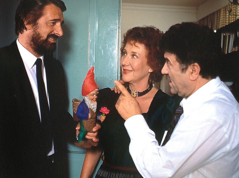 Die Hausmeisterin Martha Haslbeck (Veronika Fitz) wird mit ihrem griechischen Freund Costa (Janis Kiriakidis, links) nun anscheinend tatsächlich das Häuschen im Grünen beziehen. Ex-Ehemann Josef (Helmut Fischer) überreicht ein Abschiedsgeschenk. – Bild: BR/​BR