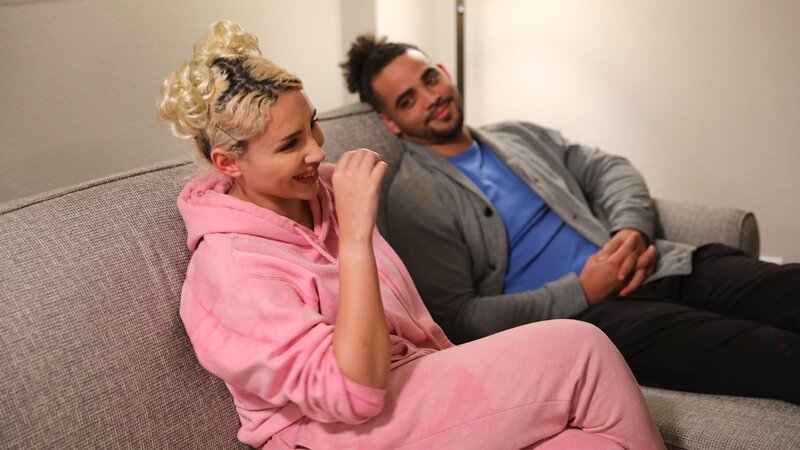 Sophie and Rob laugh while sitting on the couch in Claire’s hotel room. – Bild: Warner Bros. Discovery, Inc. or its subsidiaries and affiliates. All rights reserved.