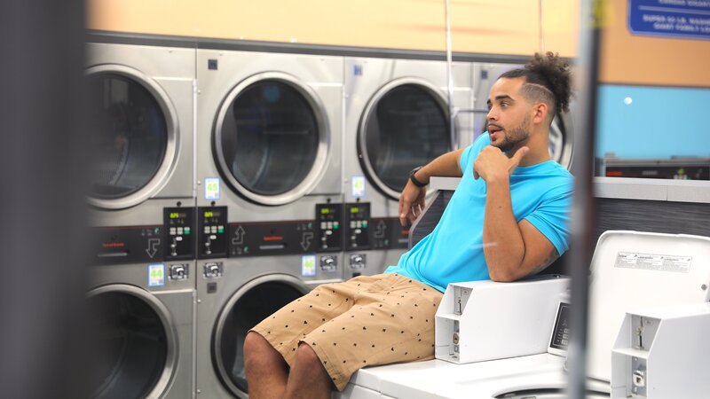 Rob sits on a washing machine in a laundromat while talking to his friends Ty and Tor’i. – Bild: 2023 Warner Bros. Discovery, Inc. or its subsidiaries and affiliates. All rights reserved.
