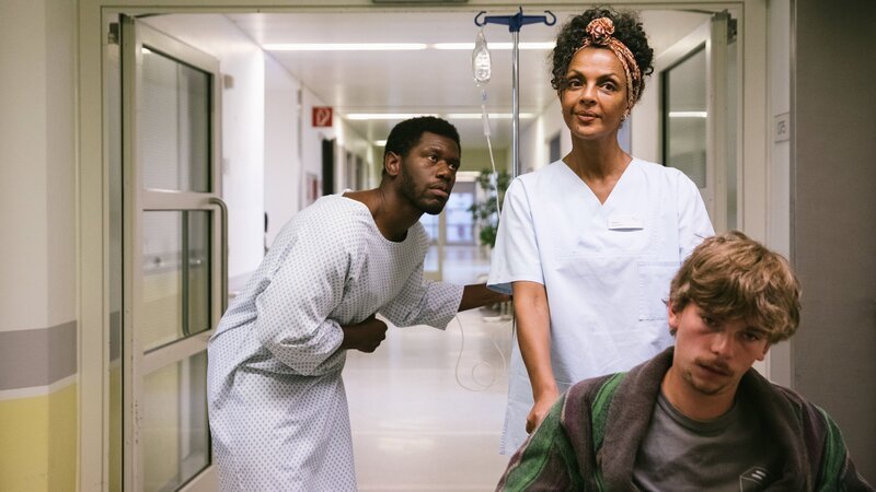 Dawit (Akeem van Flodrop, l.) ist im Stress und da kommt es ihm ganz gelegen, dass er aus Versehen Kalkentferner getrunken hat und im Krankenhaus eine Pause einlegen kann. Alle sind besorgt und denken, er wollte sich umbringen. Doch seine Mutter Lemlem (Dennenesch Zoudé, M.) kennt sein schauspielerisches Talent. – Bild: ZDF