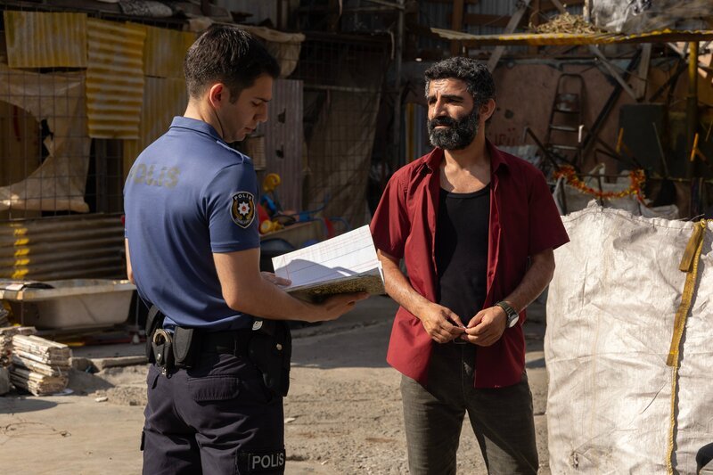 Melik (Diyar Bozkurt, l.) befragt Karim (Aziz Çapkurt), Besitzer eines Recycling-Hofs, nachdem ein toter Müllsammler gefunden wurde. – Bild: aliguler