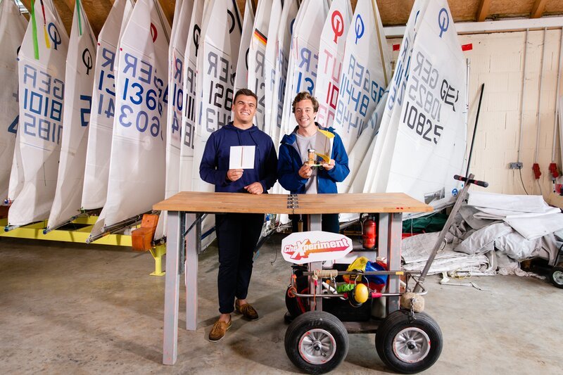 Tobi (rechts) mit seinem Herausforderer Jannik am Münchner Yachtclub Starnberg. Tobis Aufgabe: Das Segelboot knapp 30 Meter bei absoluter Windstille segeln. – Bild: BR/​megaherz gmbh/​Mathias Hagn/​Mathias Hagn