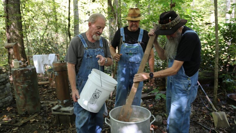 Eric „Digger“ Manes, Mark Ramsey, and Jacob „JB“ Rader making mash at the still site in the woods. – Bild: Warner Bros. Discovery