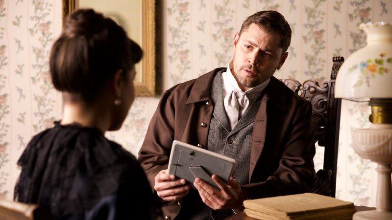 Man holds framed photograph and looks at his wife – Bild: Warner Bros. Discovery
