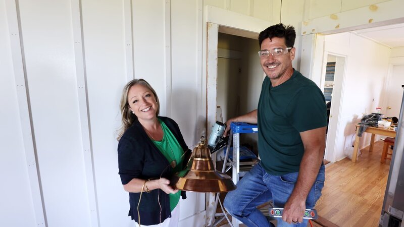 Jonathan Knight and Kristina Crestin in the living room during construction posing with a light fixture and tools, as seen on Farmhouse Fixer, Season 3. – Bild: Warner Bros. Discovery