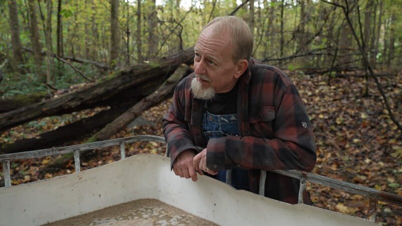 Eric „Digger“ Manes standing over a tote full of mash at the still site in the woods. – Bild: Warner Bros. Discovery