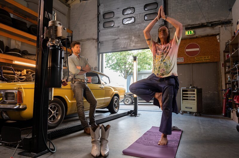 Yoga ist nicht jedermanns Sache: Kriminalkommissar Jo Stoll (Peter Ketnath, l.) steht dem neuen Hobby seines Kumpels Karl-Heinz-Schrothmann (Michael Gaedt, r.) skeptisch gegenüber – auch weil in dem Yogastudio, das Schrotti besucht, ein Yogalehrer tot aufgefunden wurde. Und tatsächlich manövriert sich der Kfz-Mechaniker tiefer in den Mordfall, als ihm lieb ist. – Bild: MARKUS_FENCHEL