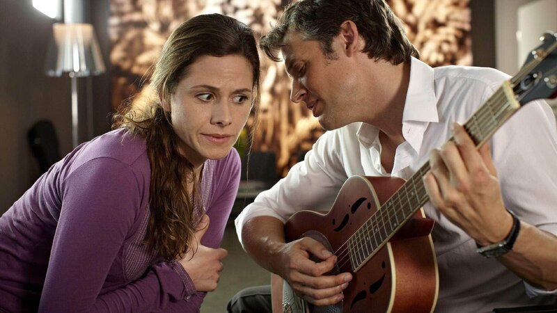 Schoener (Thorsten Feller) spielt Katja (Ellenie Salvo Gonzalez) sein selbstgeschriebenes Lied für das Firmenjubiläum vor. Doch ihr negatives Urteil wird von Schoener leider missverstanden. – Bild: MG RTL D /​ Guido Engels