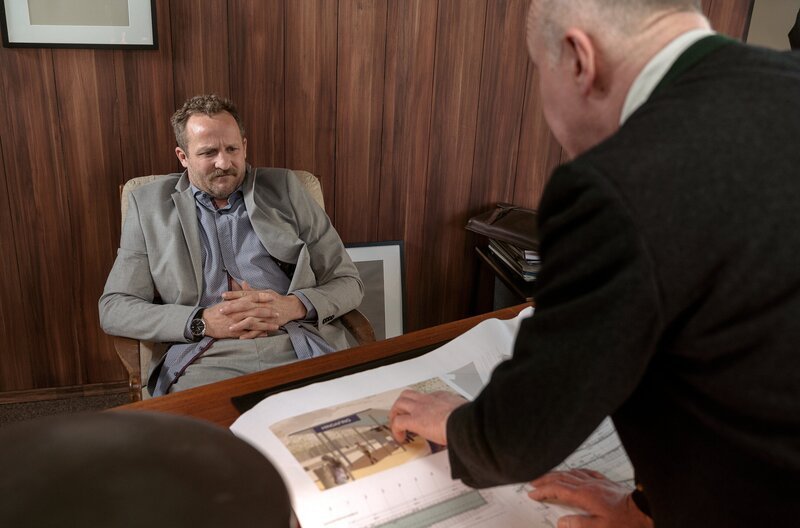 Karli Spitz (Heinz Josef Braun, rechts) zeigt Alfons Zischl (Maximilian Brückner) die Pläne für seinen Hindafinger Bahnhof. – Bild: BR/​Neuesuper Produktions GmbH/​Arvid Uhlig