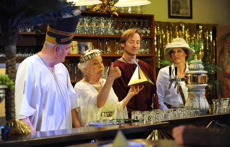 Theresa gibt sich zu Fasching als ägyptische Göttin. Von links: Joseph Brunner (Wilhelm Manske), Theresa Brunner (Ursula Erber), Gregor Brunner (Holger M. Wilhelm) und Annalena Brunner (Heidrun Gärtner). – Bild: BR/​Marco Orlando Pichler