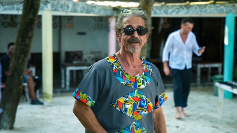 Heino stands at the barbecue table wearing sunglasses, looking forward to the test cookout – Bild: Warner Bros. Discovery