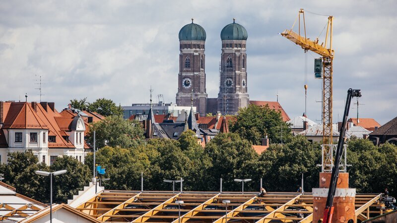 Ein Blick über das Oktoberfestgelände bis zu den beiden Türmen der Frauenkirche während der Aufbauarbeiten für das Oktoberfest. – Bild: Fabian Stoffers /​ BR
