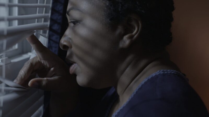 A woman peers out of blinds. – Bild: Investigation Discovery /​ Discovery Communications