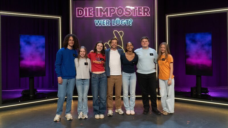 Moderator Tobias Krell (Mitte) mit den „Swifties“. Doch zwei Imposter mischen sich ins Spiel. Wer sind die wahren Fans? – Bild: hr/​Bavaria Entertainment/​dyrdee Media GmbH & Co. KG