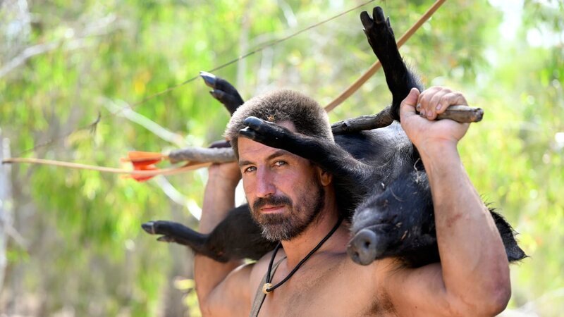 Matt stands with a slain pig across his back, looking into the camera. – Bild: Warner Bros. Discovery