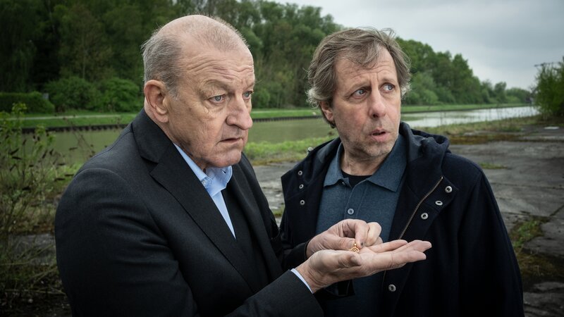 Privatdetektiv Georg Wilsberg (Leonard Lansink, l.) zeigt Ekki Talkötter (Oliver Korittke, r.) einen wichtigen Fund – führt die Goldkette zur Lösung des Rätsels um den verschwundenen Bräutigam? – Bild: ZDF/​Thomas Kost