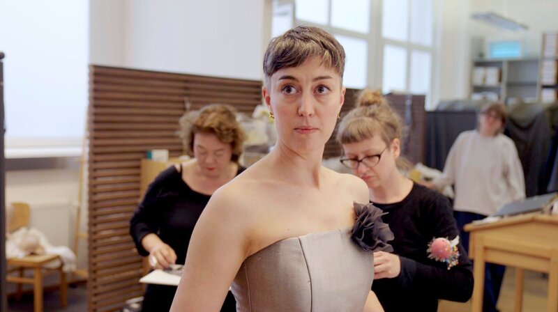 Der Film begleitet Sängerinnen und Sänger, Chor, Gürzenich-Orchester, Kostüm, Bühnenbild und Bühnentechnik. Sie erzählt von Erinnerungen, Hoffnungen und Enttäuschungen – und von der Frage, was ein Ort mit den Menschen macht, die dort arbeiten. Richard Strauss’ „Der Rosenkavalier“ ist die erste Premiere im neuen alten Haus. Plötzlich geht es nicht mehr um die Baustelle, sondern darum, wie dieser Ort wieder zum Leben erwacht. Bianca Andrew, Mezzosopranistin, bei der Anprobe. – Bild: WDR/​Bildersturm Filmproduktion GmbH