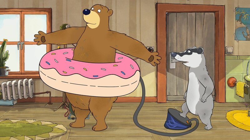 Dr. Brumm trägt einen Schwimmring um den Bauch, der von Dachs aufgepumpt wird. – Bild: rbb/​MDR/​NDR/​TRIKK17