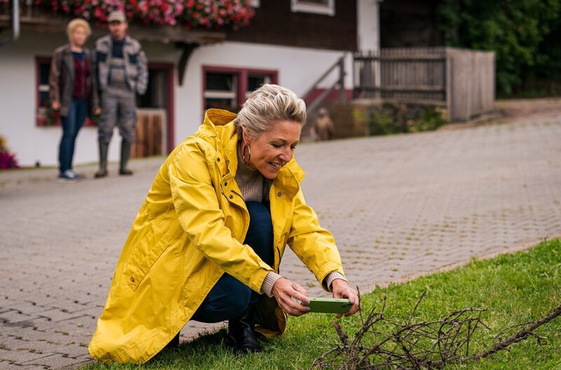 Eine geheimnisvolle Frau erscheint auf dem Hof und macht ungefragt Fotos von allen möglichen Dingen. Bea (Christiane Brammer) und Sebastian (Dominik Stricker) rätseln über die Unbekannte und sprechen sie an. Es ist Aurelia (Alexandra Hofmann), eine Künstlerin. – Bild: SWR/​Christian Koch